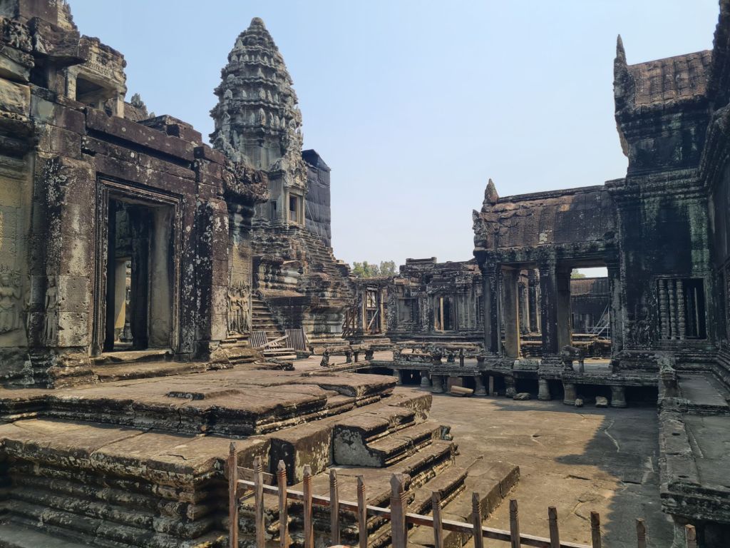 Ruins of ancient temple complex with stone structures, stairs, and detailed carvings under a clear blue sky.