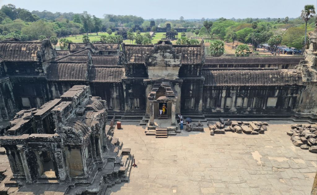 Aerial view of the ancient Angkor Wat temple complex, showcasing its intricate stone architecture and surrounding greenery, with tourists exploring the site.