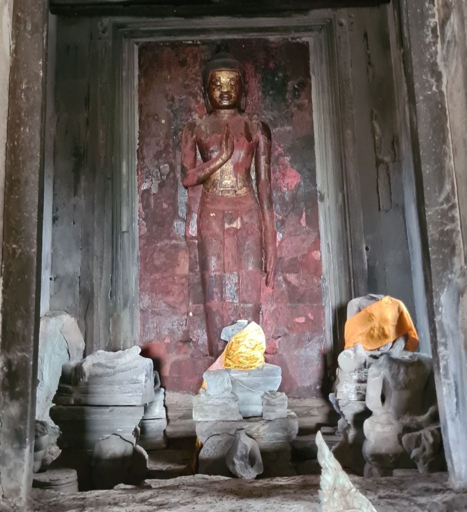An ancient Buddha statue in a stone alcove, surrounded by weathered stone offerings and partially covered with orange cloth.