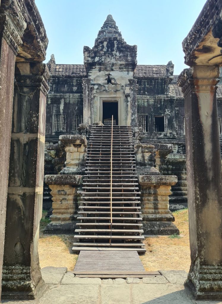 Stone staircase leading to the entrance of an ancient temple, framed by two pillars, with detailed architecture visible on the temple facade.