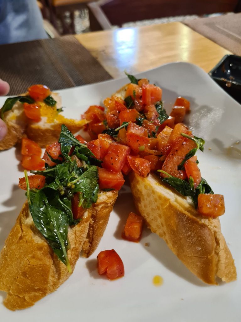 Plate of bruschetta topped with diced tomatoes and fresh basil, featuring toasted bread slices.