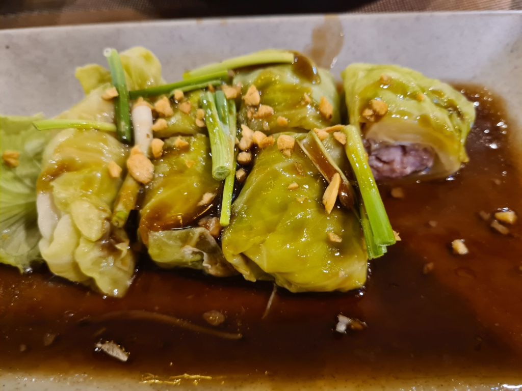 Cabbage rolls filled with minced meat, topped with chopped peanuts and green onions in a savory sauce.