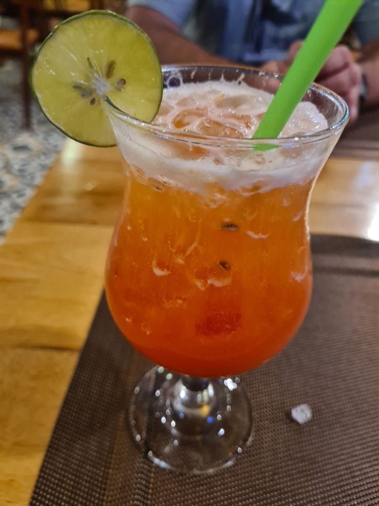 A vibrant cocktail served in a glass with ice, garnished with a slice of lime and a green straw, resting on a textured surface.