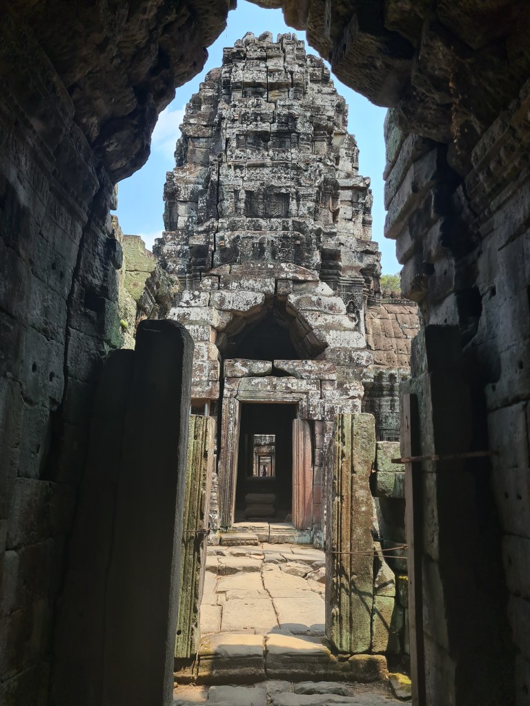 View through a stone archway leading to a temple tower, featuring intricate carvings and a pathway of weathered stone slabs.