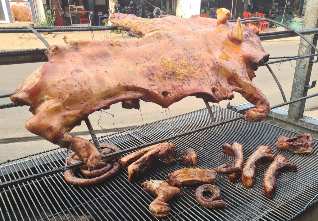 A whole roasted pig hanging on a grill, with various cuts of meat and sausages displayed on the grate below.