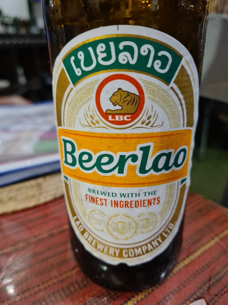 Close-up of a Beerlao beer bottle featuring its label with Laotian script, the logo of LBC, and a depiction of a tiger.