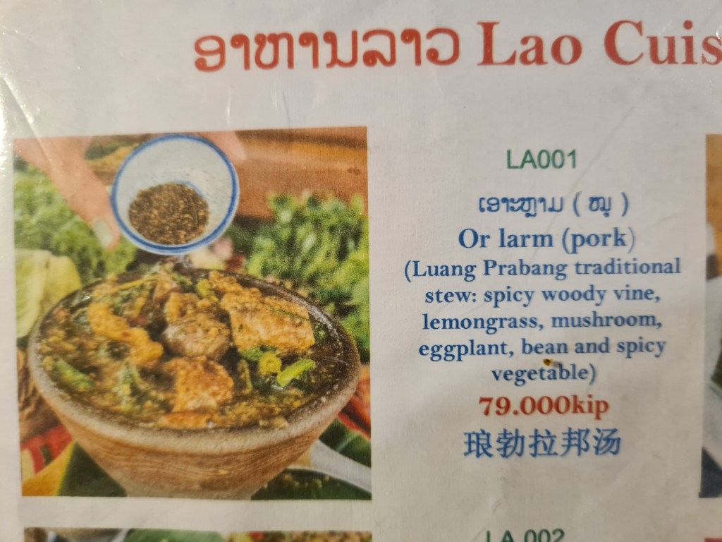 A menu item featuring Lao cuisine, specifically a traditional dish called 'Or larm' (pork stew) with ingredients like spicy woody vine, lemongrass, mushrooms, eggplant, beans, and spicy vegetables. The price is displayed as 79,000 kip.
