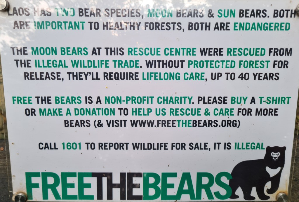 Information sign about Moon Bears at a rescue center in Laos, emphasizing their importance to forests, their endangered status, and the illegal wildlife trade. It promotes the non-profit charity 'Free The Bears' and encourages donations and purchases to support bear rescue efforts.