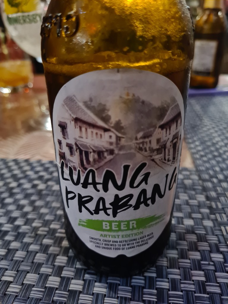 Close-up of a Luang Prabang beer bottle featuring an artist edition label with a vintage illustration of buildings
