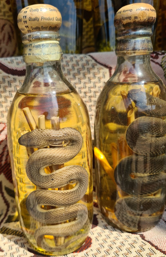 Two glass bottles containing snakes submerged in yellow liquid, displayed on a patterned fabric background.