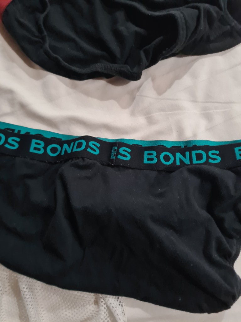 Close-up of black underwear with a turquoise 'BONDS' waistband, resting on a light-colored surface.
