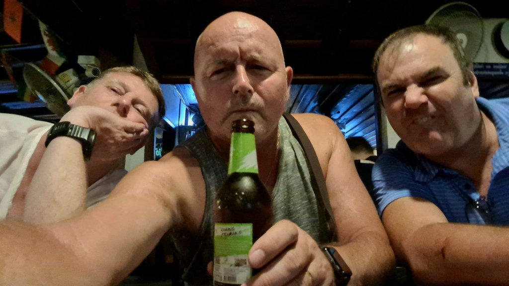 Three men making funny faces while sitting at a bar, one holding a beer bottle.