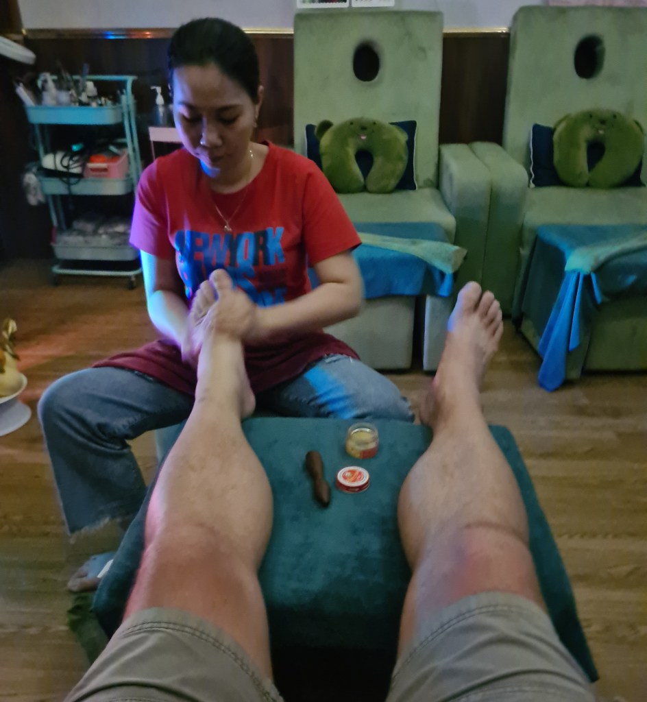 A woman giving a foot massage to a person sitting in a chair, with the focus on their feet and the massage process.
