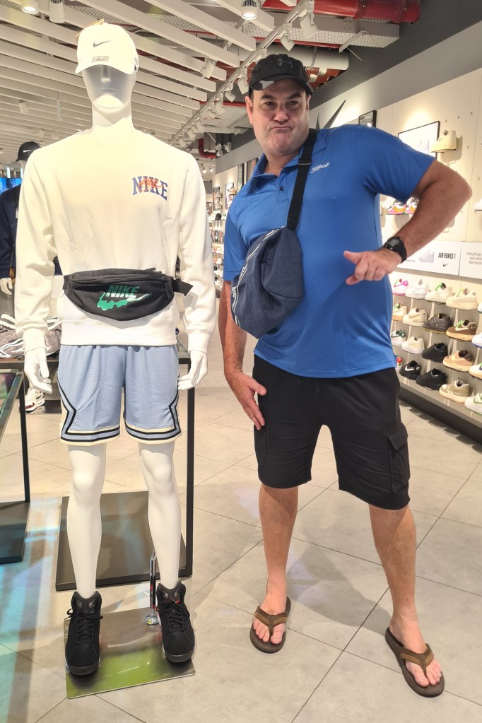 A mannequin dressed in a Nike outfit stands beside a man posing playfully in a sports retail store.