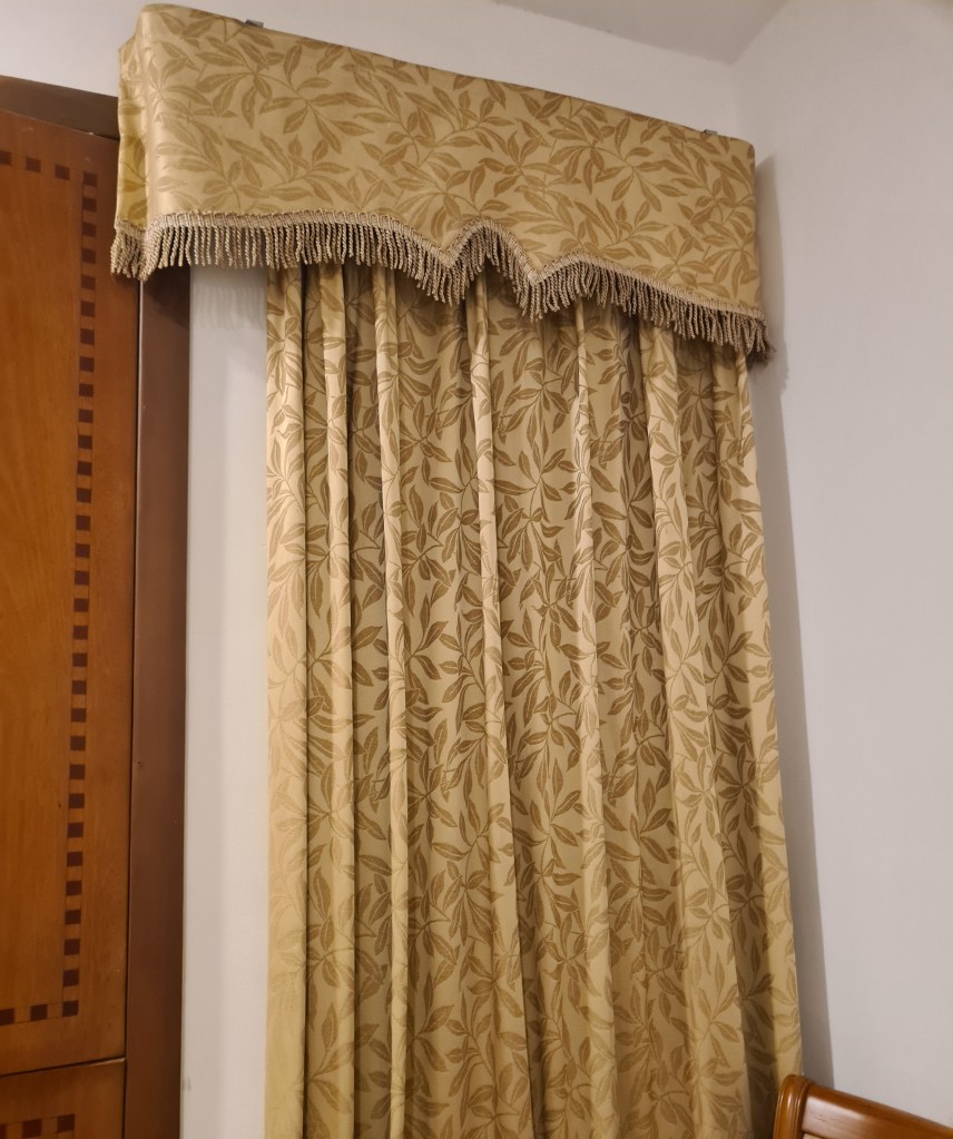 Elegant golden curtains with a floral pattern and a decorative valance, hanging beside a wooden cabinet.